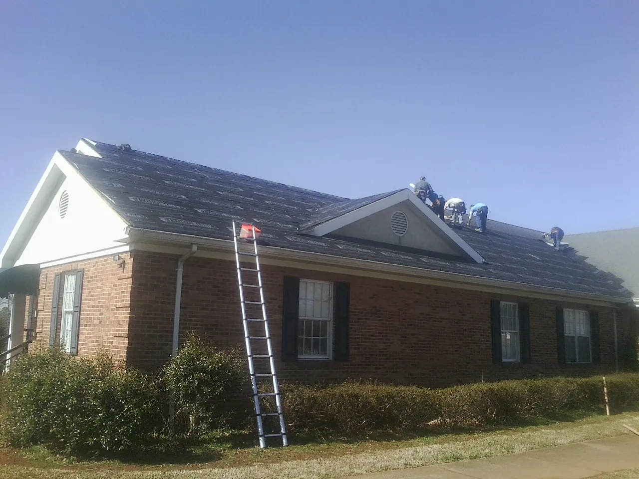 Crew tearing shingles off a brick ranch roof with a ladder set — Metal Roof Repair work by our crew in Basin