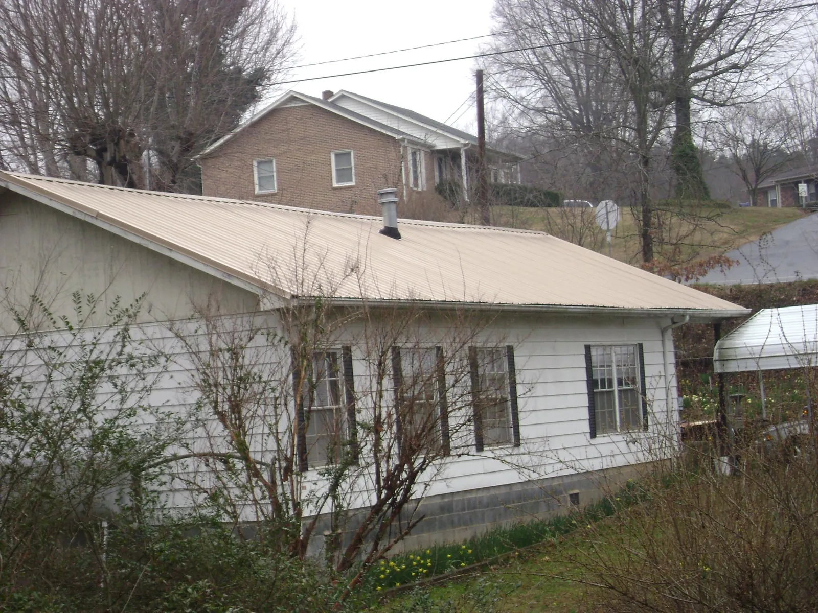 Tan metal roof on a white sided house set into a hillside — Commercial Roofing by Roofing Brothers in Basin