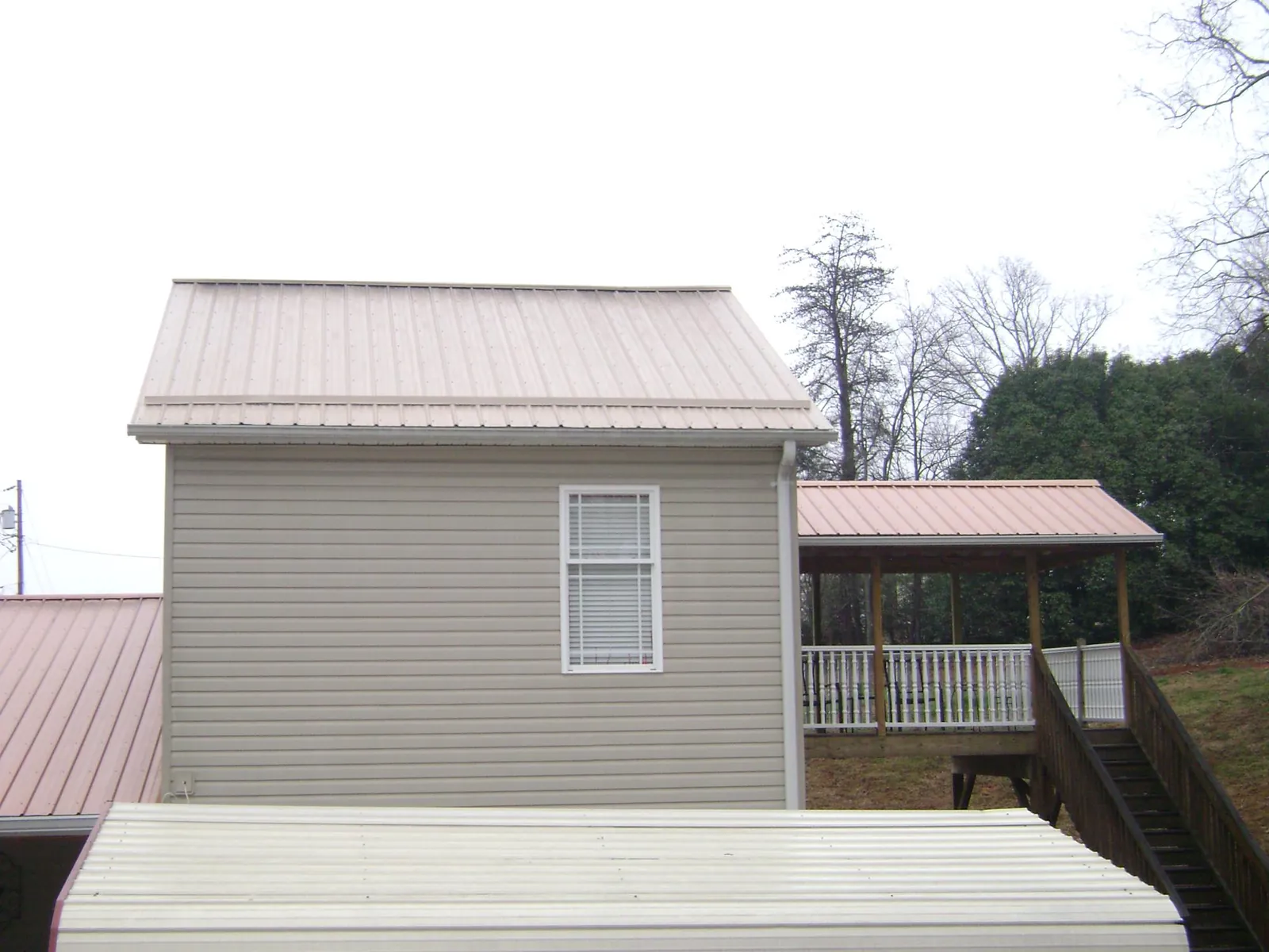 Tan metal roofs on a two story addition and attached porch, from a Roof Replacement job in Basin